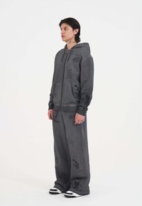 Sudadera con capucha gris y cremallera, con diseños gráficos negros, combinada con pantalones anchos a juego. Acentuada con calzado rayado en blanco y negro.