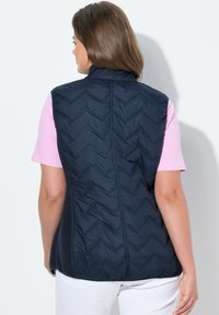 Chaleco acolchado azul marino con un alto cuello, con costuras en espiga, combinado con una camiseta de color rosa claro. Textura suave, diseño sin mangas.
