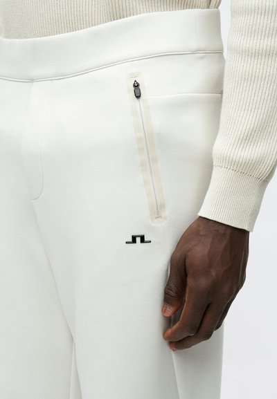 Λευκά φούτερ παντελόνια με απαλή υφή ύφανσης, με πλαϊνή τσέπη με φερμουάρ και μικρό μαύρο λογότυπο. Απλός, κομψός σχεδιασμός.