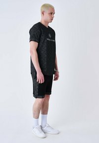 Ensemble t-shirt graphique noir et short avec un motif géométrique, présentant un détail de logo, associé à des baskets blanches et des chaussettes mi-mollet.
