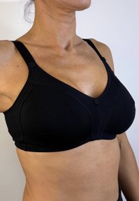 Sujetador de algodón negro con copas suaves, tirantes ajustables y adornos decorativos de flores cerca de los tirantes. Presenta un diseño de escote en V y una textura suave.