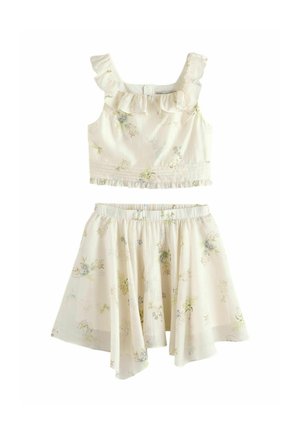 Kremowy dwuczęściowy strój z falbanianym, bezrękawnym krótkim topem i dopasowaną rozkloszowaną spódnicą, oba elementy ozdobione delikatnym kwiatowym wzorem.
