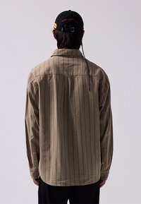 Long-sleeve, olive green shirt with vertical stripes, button-down collar, and a relaxed fit. Crafted from textured fabric with a rear yoke.