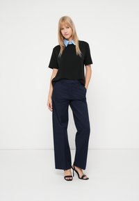 Top negru cu mâneci scurte, guler bleu deschis, asortat cu pantaloni evazați bleumarin și sandale negre cu toc înalt. Design simplu și curat.