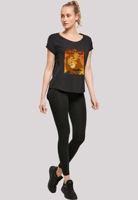 Svart T-skjorte med rund hals og en fargerik Lion King-grafikk. Kombinert med svarte leggings og svarte joggesko.
