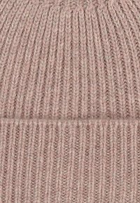 Knitted beanie in soft, light pink yarn with ribbed texture. Features a folded cuff and distinct vertical patterns throughout.
