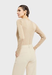 Dugi rukav, prilagođen top od metalik bež tkanine; glatka tekstura s minimalističkim šavovima, nosi se s visokim bež hlačama.