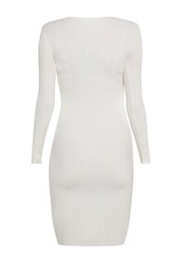 Långärmad, ribbad klänning i vitt. Figursydd design, hög krage och slät yta. Knälång med åtsittande ärmmuddar. Inga dekorativa detaljer.