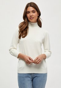 Baltas megztinis su aukštu kaklu, ilgomis rankovėmis, raukšlėtomis rankogaliais ir apvadu, minkšta tekstūra; derinamas su šviesiai mėlynomis džinsomis. Minimalus dizainas, kasdienis stilius.