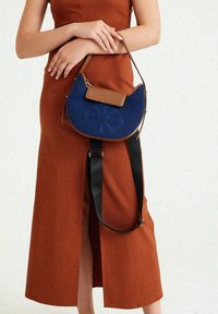 Blaue Lederhandtasche mit geschwungener Form, braunen Akzenten und einem strukturierten Blumenmuster. Verfügt über einen abnehmbaren schwarzen Tragegurt.