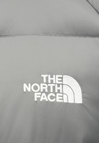 Szürke, szigetelt dzseki, amelynek figyelemfelkeltő, fehér hímzett logója van a "The North Face" felirattal, ívelt ívformában. Puha anyagú textúra.