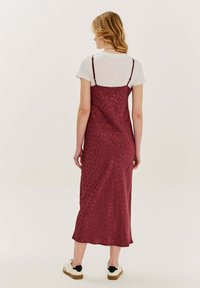 Bordová šaty bez rukávov s tenkými ramienkami, kvetinovým vzorom a ľahkou textúrou, vrstvené cez biele tričko. Zahrnuté sú aj pohodlné kotníkové topánky.