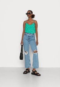 Camisola de alças com padrão floral verde, calças largas rasgadas azul claro, sandálias de plataforma pretas e uma pequena bolsa preta.