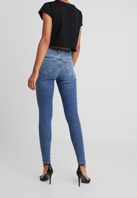 Blå denim skinny jeans med hög midja, som har en klassisk femficksdesign. Matchas med en kort svart T-shirt och svarta klackar.