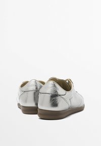 Chaussures en cuir argenté à texture lisse, forme arrondie, semelle en caoutchouc et marquage embossé au dos. Design minimaliste.