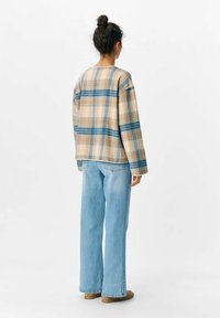 Giacca a plaid beige con accenti blu e arancioni, caratterizzata da una vestibilità rilassata e maniche ampie, abbinata a jeans svasati di un blu chiaro.