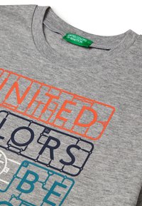 Šedé bavlněné tričko s vrstveným grafickým designem. Text "UNITED COLORS" je výrazně zobrazen na přední straně v oranžové a modré barvě.