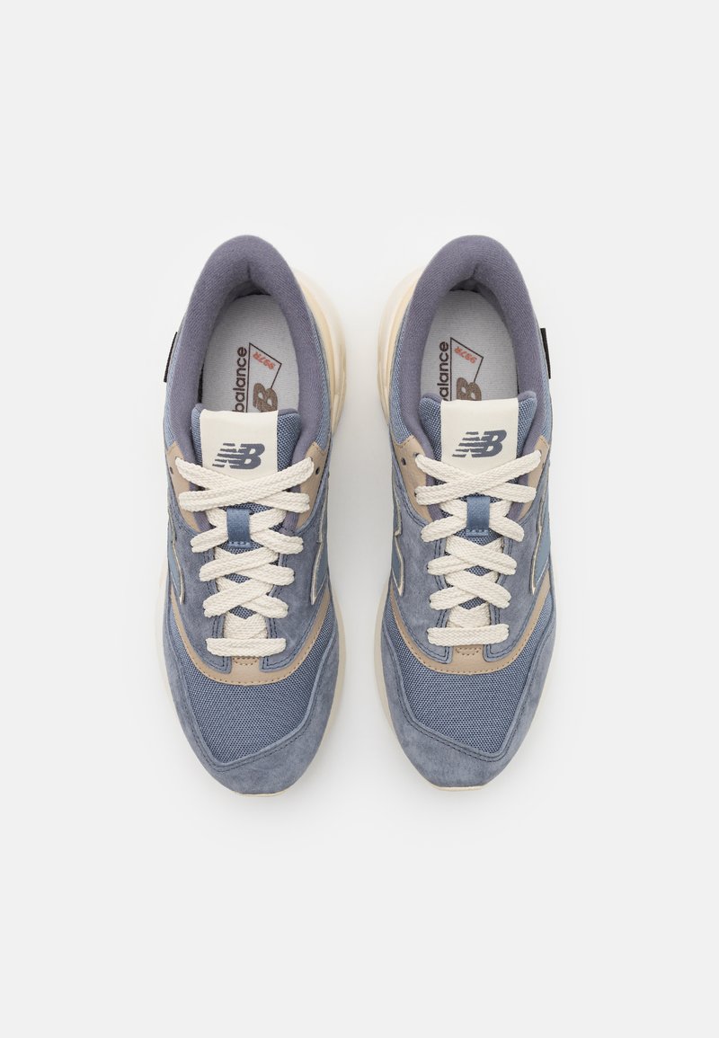 Blaue und beige New Balance Sneaker verfügen über Mesh- und Wildlederstrukturen, runde Zehen, dicke Sohlen und cremefarbene Schnürsenkel. Weißes Logo an den Seiten.
