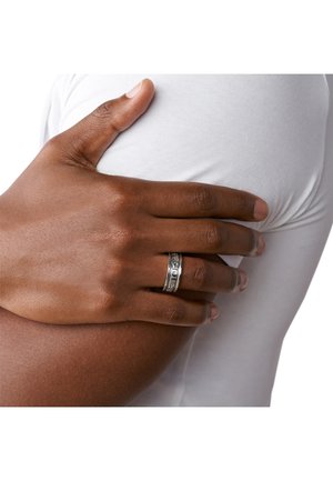 Anello d'argento con motivi intricati, indossato su una mano che riposa su una camicia bianca. Il tono della pelle è di un marrone intenso.