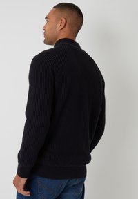 Marineblauer gerippter Pullover mit hohem Kragen und langen Ärmeln, der eine strukturierte Oberfläche und einen taillierten Bund aufweist.