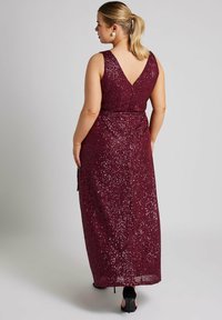 Vestido de lentejuelas burdeos con escote en V, diseño sin mangas y silueta larga hasta el suelo. Superficie texturizada y brillante con una cintura ajustada.