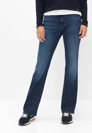 Person wearing dark blue straight-leg jeans, navy sneakers with white laces, a navy sweater, and a white shirt underneath.