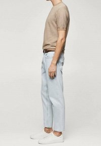 Camisa de punto beige de manga corta, jeans de corte holgado en azul claro y zapatillas blancas. Silueta ajustada; camisa texturizada, jeans ligeramente recortados en los tobillos.
