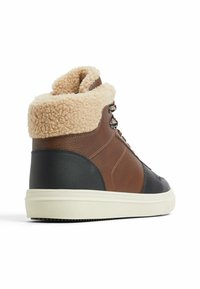 Zapatillas altas de cuero marrón con un cuello de felpa beige, panel texturizado negro y suela de goma blanca, diseñadas para la comodidad y la durabilidad.