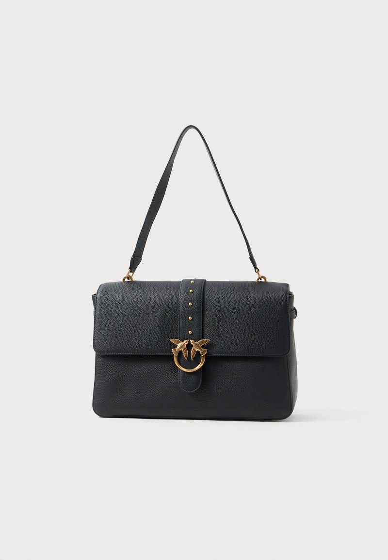 Bolsa de mão preta em couro com formato estruturado, apresentando um fecho frontal, metalizações em tom dourado, tachas decorativas e uma alça de mão superior.