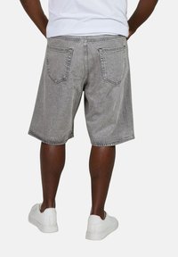Shorts in denim grigio con una vestibilità rilassata, dotati di tasche posteriori e orlo sfilacciato. Indossati con sneakers bianche, visti da dietro.
