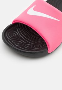 Růžové klouzavé sandály s texturovanou černou podrážkou. Mají široký pásek s bílým logem Nike. Měkký materiál s vzorovanou stélkou pro lepší úchop.