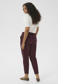 Burgundy tailored pants with a slim fit, featuring front pockets and tapered ankles. Worn with a white short-sleeve top and beige flats.