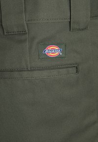 Dark green fabric label on Dickies pants, featuring a multi-colored logo with red, yellow, and blue text, stitched to the waistband.