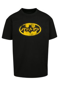 Black cotton t-shirt featuring a faded yellow Batman logo with Japanese text, round neckline, and short sleeves. No notable patterns.