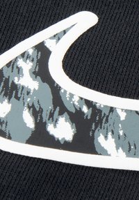 Крупен план на черна тъкан с бяло и сиво абстрактно шарено лого Nike Swoosh, очертано в бяло.
