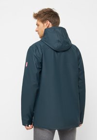 Giacca impermeabile blu navy con cappuccio, caratterizzata da una texture liscia, una silhouette aderente e dettagli in metallo argentato sui polsini.