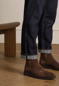 Bruine suède enkellaarsjes met een platte zool, gedragen met donkere spijkerbroeken die een opgerolde zoom hebben en contrasterende lichtblauwe stiksels.