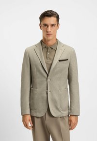 Hellgrauer Blazer aus strukturiertem Stoff, mit Revers und zwei Fronttaschen. Kombiniert mit einem passenden Hemd mit Kragen und Knöpfen.