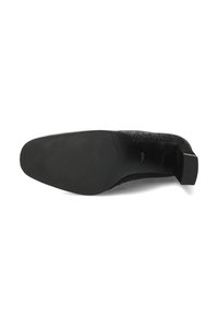 Suela de zapato negro con una textura suave, que presenta una punta redonda y un tacón bajo y cuadrado. La parte superior tiene una textura con un patrón intrincado.