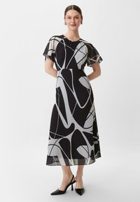 Czarna i biała sukienka z przezroczystymi, lejącymi rękawami, z abstrakcyjnymi wzorami liniowymi, dopasowanym gorsetem i swobodnie opadającą, średniej długości spódnicą.