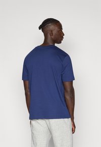 T-shirt azul-marinho de manga curta feito de algodão. Apresenta um decote redondo e um corte regular, exibido pela parte de trás. Design simples, sem padrões.