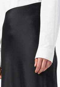 Schwarzer, eleganter Satinrock mit glatter Textur, kombiniert mit einem weißen Langarmhemd mit strukturierten Manschetten.