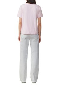 T-shirt en coton rose clair à manches courtes, associé à un pantalon large blanc, avec des poches arrière et une coupe droite.