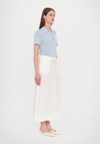 Heleheles sinine lühikeste varrukatega polo särk, millel on nööbid ja krae, paaritatud valge, pahkluuni ulatuva volditud seelikuga. Minimalistlik disain ja tekstuur.