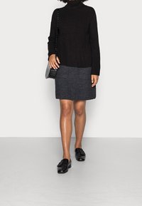 Un pull noir à col roulé rayé, une jupe à carreaux grise et des mocassins noirs avec une boucle. Un petit sac à bandoulière texturé est porté.