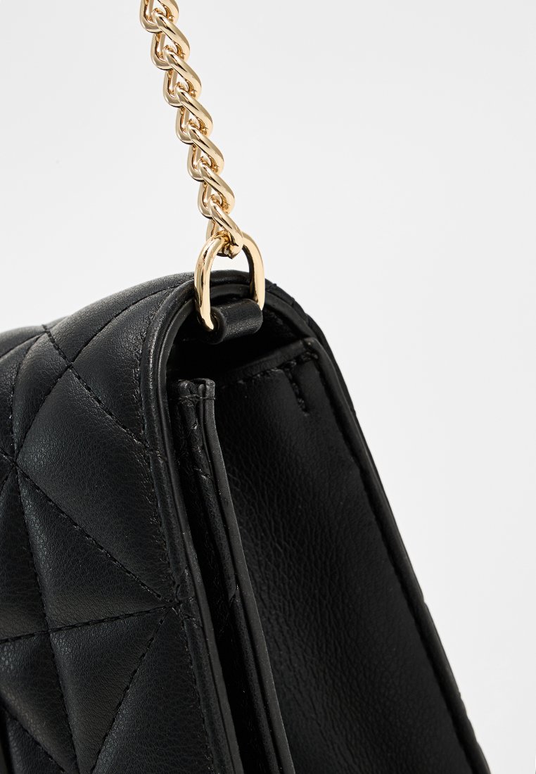 Bolso de cuero negro acolchado con una correa de cadena dorada y cierre con cremallera. Presenta un acabado texturizado y un énfasis en los detalles de costura.