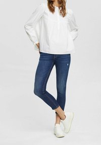 Biała bluzka z długim rękawem z guzikiem z przodu, zestawiona z ciemnoniebieskimi dżinsami skinny. Uzupełniona białymi trampkami. Prosty i casualowy design.