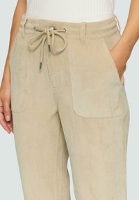 Beige corduroy broek met een trekkoord in de taille, zijzakken en een zachte textuur. Kenmerkt zich door een relaxed fit en zichtbare naden.
