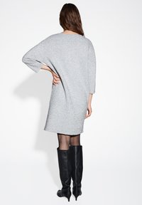 Zilveren, getextureerde oversized jurk met driekwartmouwen, een rechte snit en een zoom boven de knie, gecombineerd met zwarte laarzen tot aan de knie.