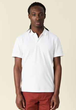Witte polo met korte mouwen, met een klassieke kraag en drie knopen. Glad oppervlak, gecombineerd met rode shorts.